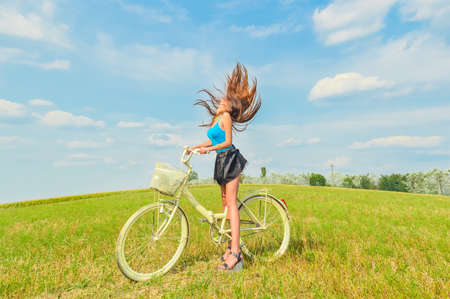 joyful cycling: sexy young pretty lady having fun enjoying freedom in fields under bright blue summer sky on green copy space background, portraitの写真素材