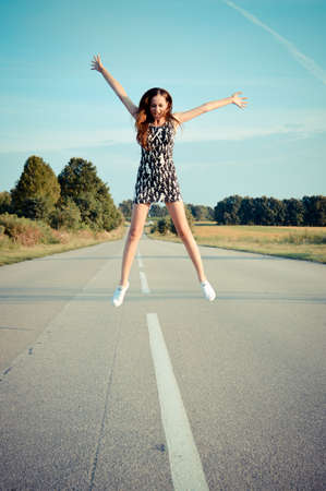 road star: portrait of beautiful brunette young woman having fun happy jump on the country road on green summer outdoors copy space backgroundの写真素材