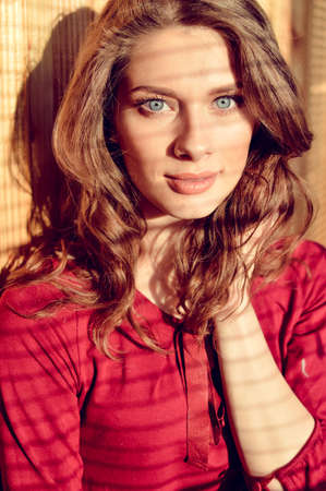 closeup portrait of gently looking at camera beautiful young blue eyes lady with shadow from window blindsの写真素材
