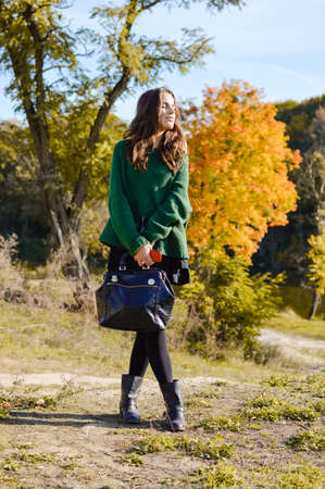 portrait of beautiful young lady with bag standing on autumn countryside road and enjoying sunshine on sunny outdoors copy space backgroundの写真素材