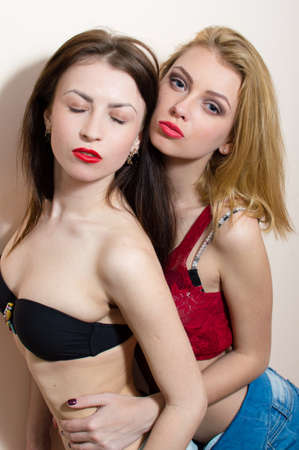 closeup portrait of 2 sexy romantic beautiful young ladies in jeans shorts having fun & good time hugging each other on light copy space backgroundの写真素材