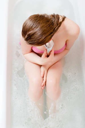 spa time: beautiful blond young woman having fun relaxing in bath holding shower on soap water copy space backgroundの写真素材