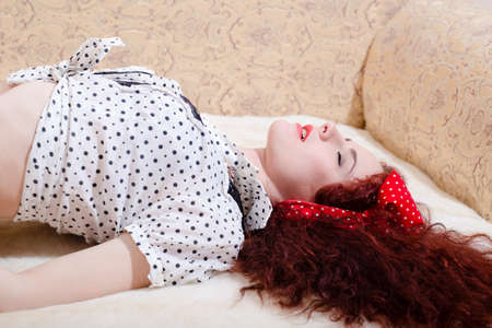 tempting beautiful red hair pinup girl having fun relaxing lying on bed sensually eyes closed on a light copy space backgroundの写真素材