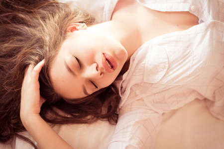 sleeping beauty: closeup portrait of young beautiful glamor woman in white shirt lying on the bed eyes closedの写真素材