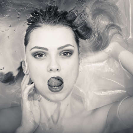 spa tongue: portrait of bathing in the water beautiful tender young blond woman having fun posing sensually & looking at camera on light copy space background, black and whiteの写真素材