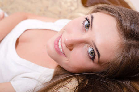 closeup portrait of young magic beautiful charming lady in white shirt lying on the bed & looking at camera happy smilingの写真素材