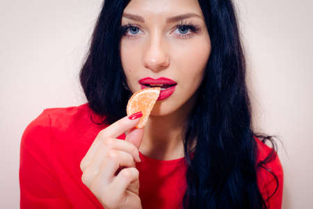 closeup picture of beautiful luxury sensual lady glamor sexy girl with seductive lips, white excellent teeth and red manicure nails eating jujube or candy on light copy space backgroundの写真素材