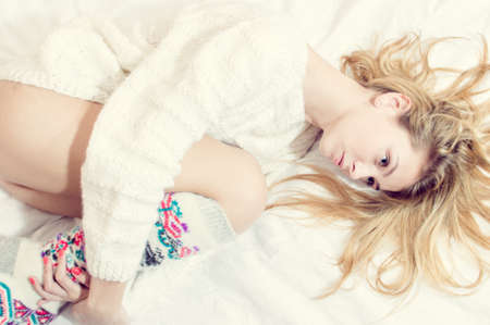 blue eyes beauty in bed: portrait of beautiful blond sexy young woman on white copy space background wearing just hand made jumper and knee socksの写真素材
