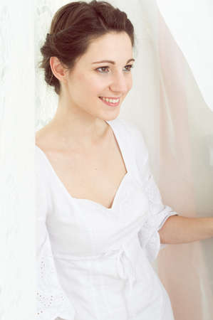 portrait of elegant beautiful young lady in white dress happy smiling on copy space tulle curtain backgroundの写真素材