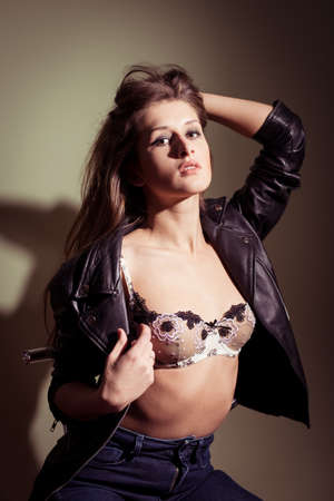 portrait of sexy beautiful young woman in leather jacket and lingerie posing and looking at camera over light copy space backgroundの写真素材