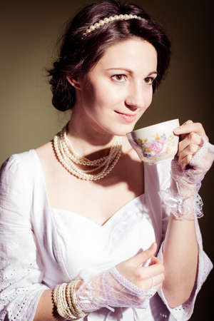 portrait of drinking tea or coffee beautiful young lady in white dress having fun happy smile on copy space backgroundの写真素材