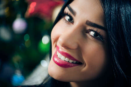 portrait of young beautiful brunette woman happy smiling & looking at camera on Christmas tree backgroundの写真素材