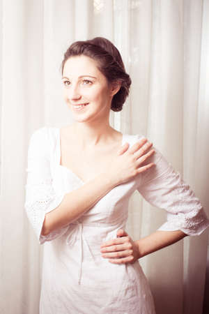 portrait of elegant beautiful young lady in white dress happy smiling & looking up on copy space tulle curtain backgroundの写真素材
