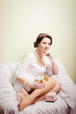 portrait of elegant beautiful young lady in white dress having fun holding present boxes and golden clock happy smile on copy space backgroundの写真素材