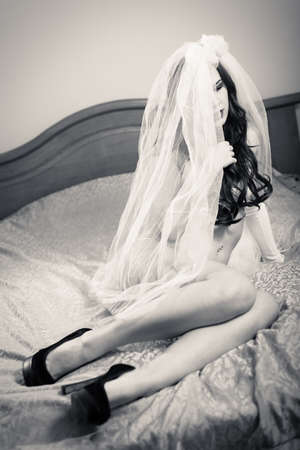 Hiding in veil beautiful sensual young lady in white lingerie relaxing in bedの写真素材