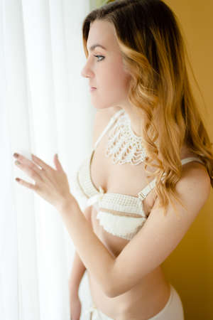 Close up portrait of beautiful young lady in white lingerie relaxing looking out the window on copy space backgroundの写真素材