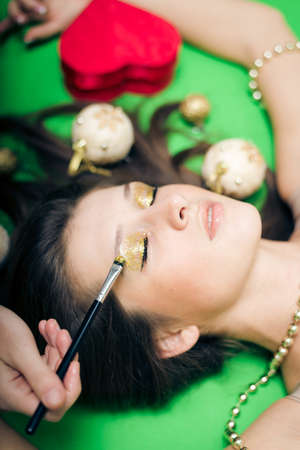 Closeup on beautiful young lady with eyes closed having fun relaxing laying down and enjoying makeup procedure on green backgroundの写真素材