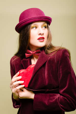 Portrait of elegant beautiful young lady hiding or taking out from coat red present box in the form of heartの写真素材