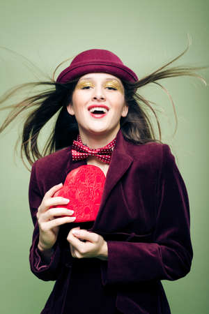 Portrait of elegant beautiful young lady hiding or taking out from coat red present box in the form of heartの写真素材