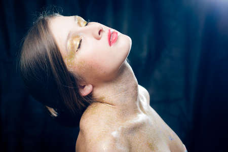 Closeup portrait of covered in shining make up sexy beautiful young woman with eyes closed relaxing on black backgroundの写真素材