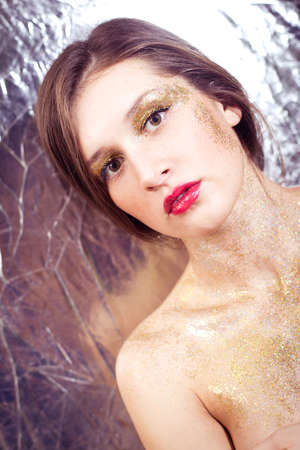 Closeup portrait of sexy beautiful young woman covered in shining make up on silver backgroundの写真素材