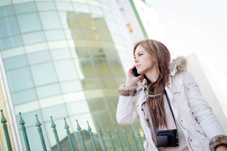 Portrait of beautiful young lady speaking on mobile phone on city glass building backgroundの写真素材