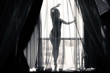 Black and white portrait of sexy beautiful young lady relaxing over light window backgroundの写真素材