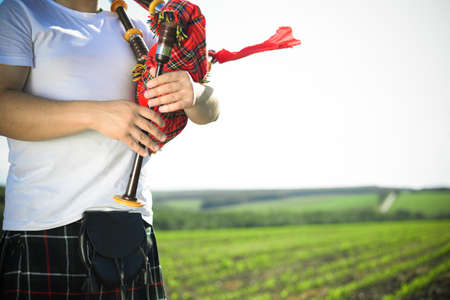 Closeup picture of young man playing pipes in national uniform on green summer outdoors copy space backgroundの写真素材