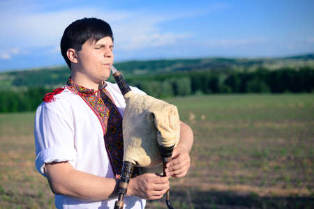 Picture of young man playing pipes on green summer outdoors copy space backgroundの写真素材