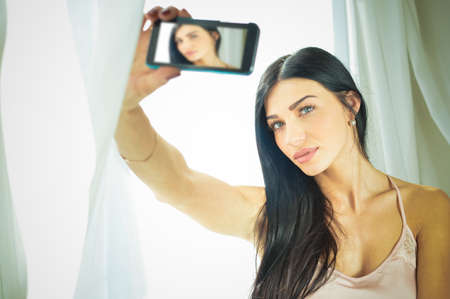 Close up portrait of beautiful young lady taking self picture at the window