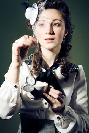 Portrait of beautiful young lady with cup of drink and pocket watch on light backgroundの写真素材