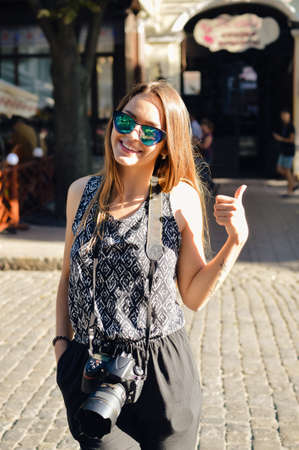 Stylish pretty girl in sunglasses with modern camera doing tourism in cityの写真素材