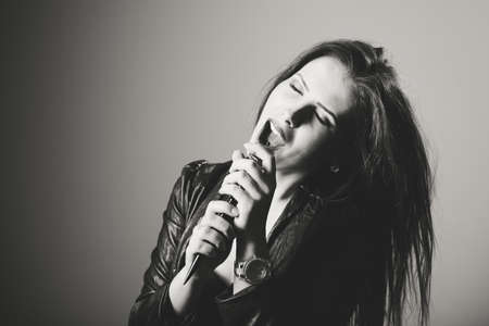 Closeup black and white portrait of pretty singing woman with closed eyes using hairbtush instead of microphoneの写真素材