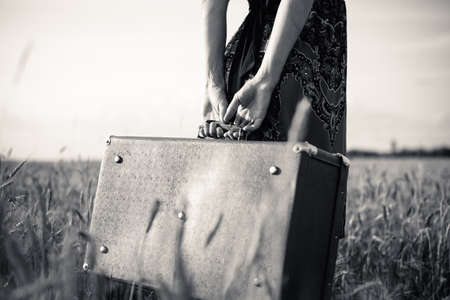 Black and white picture of slim female's arms holding retro suitcase outdoorsの写真素材