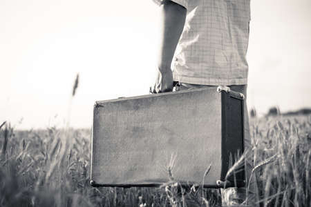 Black and white picture of man's hand holding retro suitcase outdoors over rural backgroundの写真素材