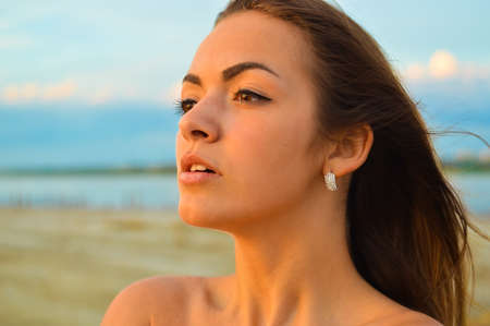 Close up picture of young brunette sensual  pensive lady on beach by sea at sunsetの写真素材