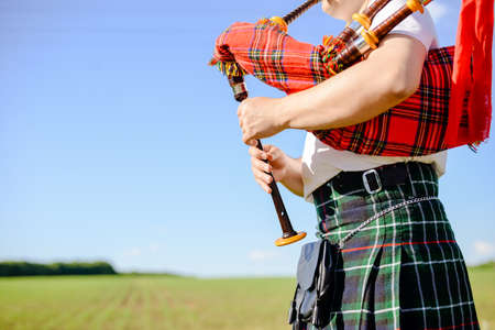 Closeup picture of male in Scottish traditional kilt playing bagpipe on green summer outdoors background Closeup picture of male in Scottish traditional kilt playing bagpipe on green summer outdoors background