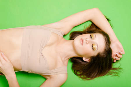 Portrait of glamour brunette girl with golden maleup lying on light green background. Horizontal photo with sexy model.の写真素材