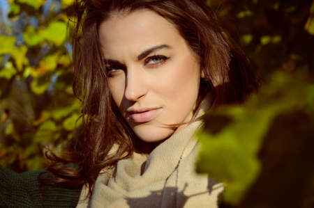 Portrait of charming woman in beige warm scarf. Closeup of young girl smiling on sunny outdoor...