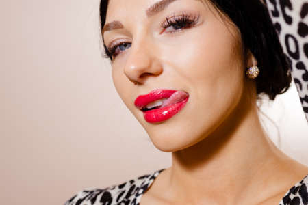 Portrait of beautiful young lady in animal print top licking her lips. Sexy girl with red lips looking at camera on beige background.の写真素材