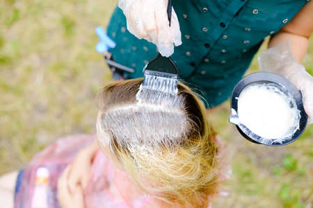 Picture of hairdresser coloring client's head using brush and bowl with due. Closeup of hands in gloves and professional equipment on summer outdoor background.の写真素材