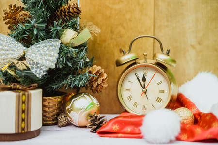 Picture of little christmas tree decorated with bows and pine cones. Artificial tree, old alarm clock and santa hat on wooden indoor background.の写真素材