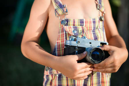Closeup picture of vintage camera which is holding by child hands. Boy wearing plaid romper in summer countryside.の写真素材