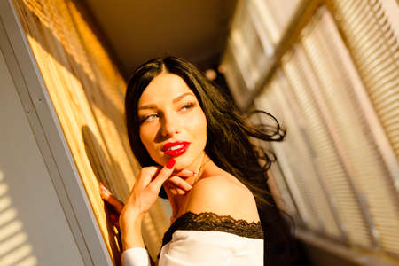 Portrait of beautiful sexy girl with red lips on balcony in sunny day. Sunlight through jalousie shines on woman's face.の写真素材