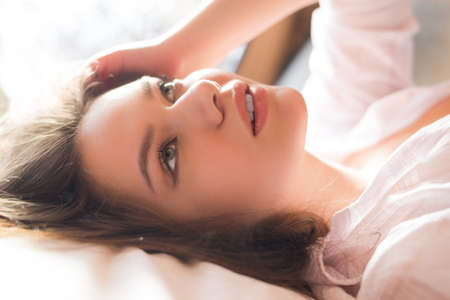 Picture of gently looking up amazing young lady laying in bed in morning sunlight. Charming girl on...