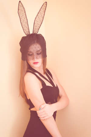 Portrait of sexy pretty girl wearing black dress and lace bunny ears. Young woman looking down in monochrome photo.の写真素材