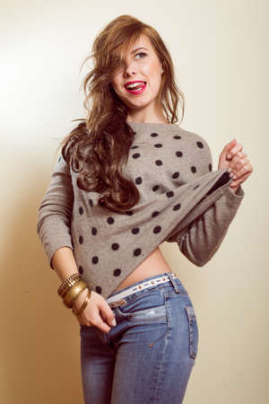 Portrait of happy young beautiful woman in jeans with raised hand. Girl wearing sweater in dark dotsの写真素材