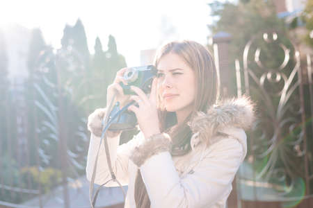 Portrait of tourist beautiful female taking photos in the city centre. Pretty girl in white jacket...