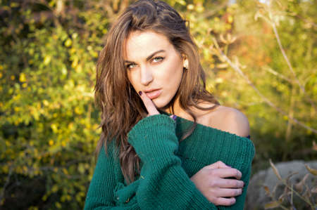 Portrait of young beautiful woman with tangled hair in big green sweater. Pretty girl looking at camera on sunny countryside background.の写真素材