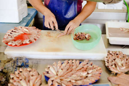 Picture of worker's hands preparing fresh fish in marketplace. Man in blue apron with knife cutting seafood ob blurred indoor background.の写真素材